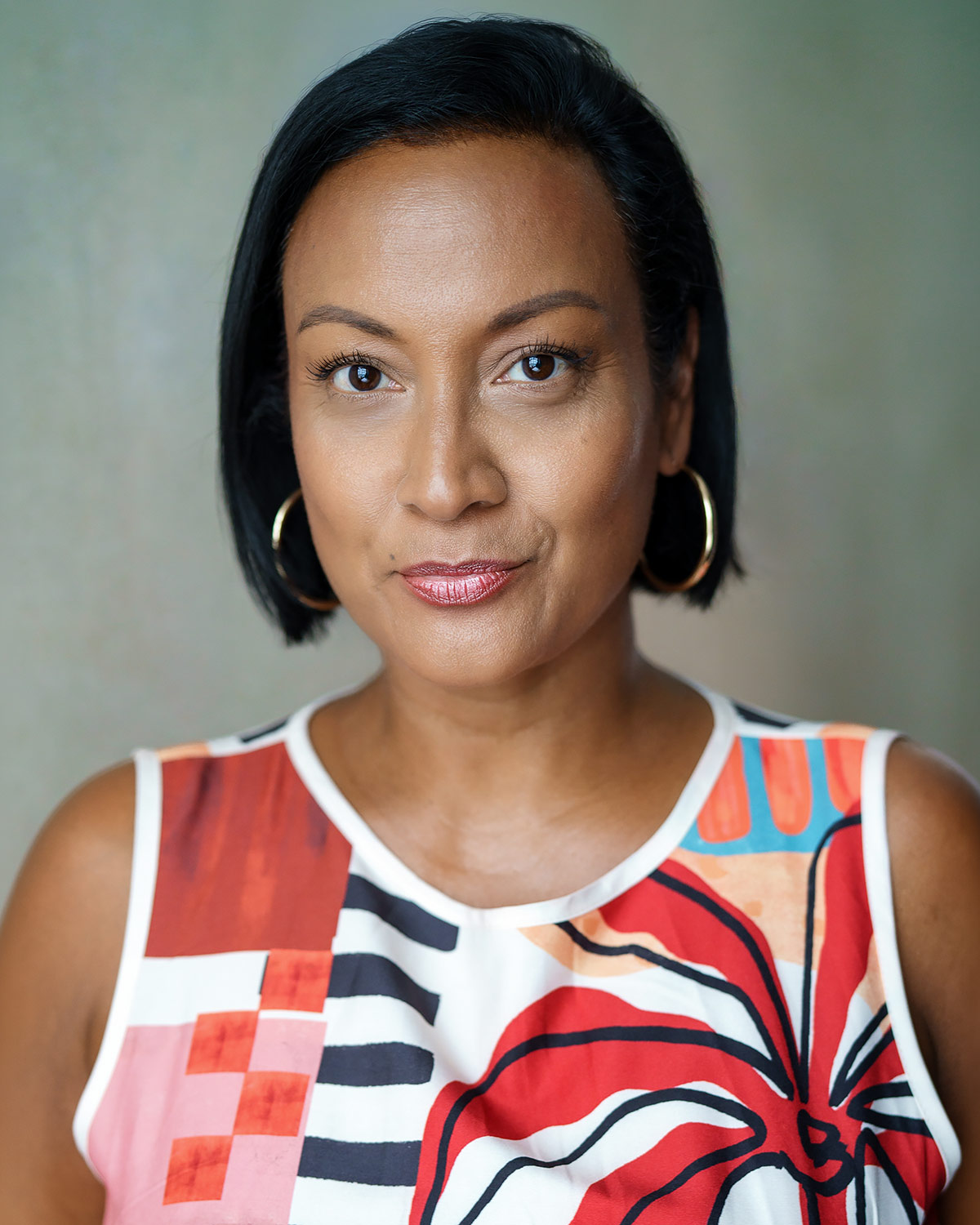 Portrait of Theresa Godly facing the camera, wearing a colourful printed top against a soft green background